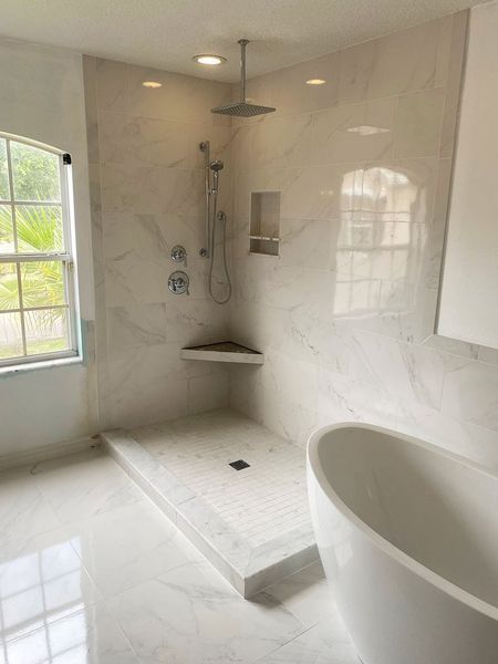 Modern bathroom with marble shower, built-in shelf, showerhead, corner seat, and freestanding tub.