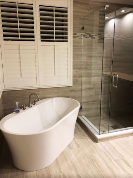 Modern bathroom: white freestanding tub, glass shower, and shuttered window.