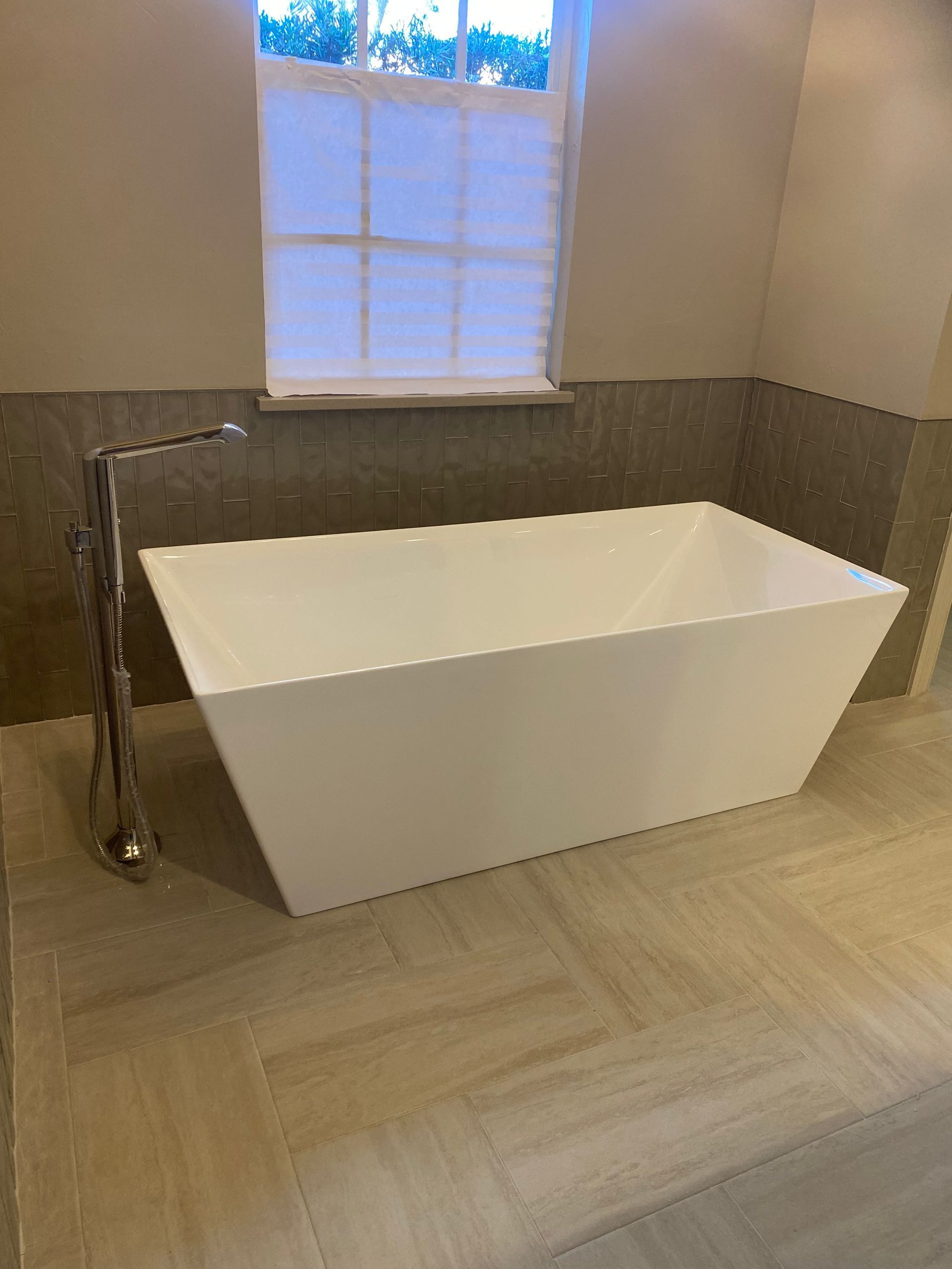 White rectangular bathtub in a bathroom with beige tile floor and a window.
