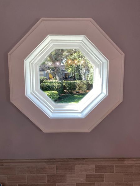 Octagon window with white trim, view of green trees and yard.