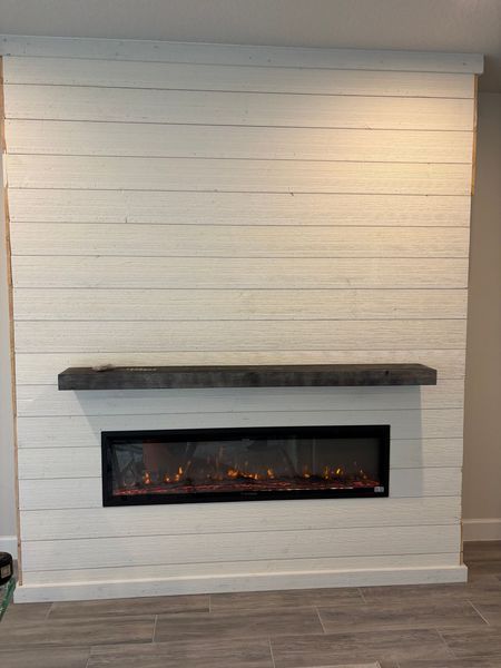 White shiplap accent wall with a built-in electric fireplace and dark wooden mantel.