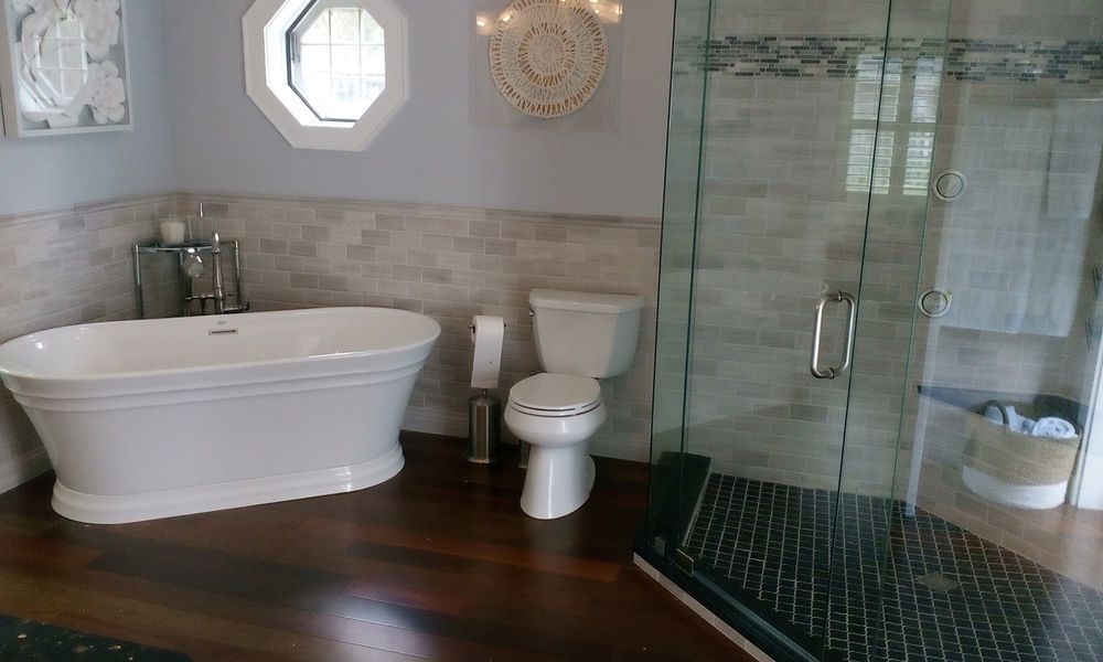 Bathroom with white freestanding tub, shower, and toilet; dark wood floor, light gray walls.