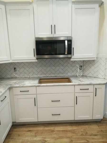 White kitchen cabinets with black hardware, microwave, and marble backsplash.