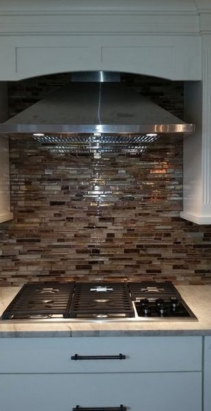 Kitchen stove with a stainless steel range hood. Brown and tan mosaic backsplash. White cabinets.