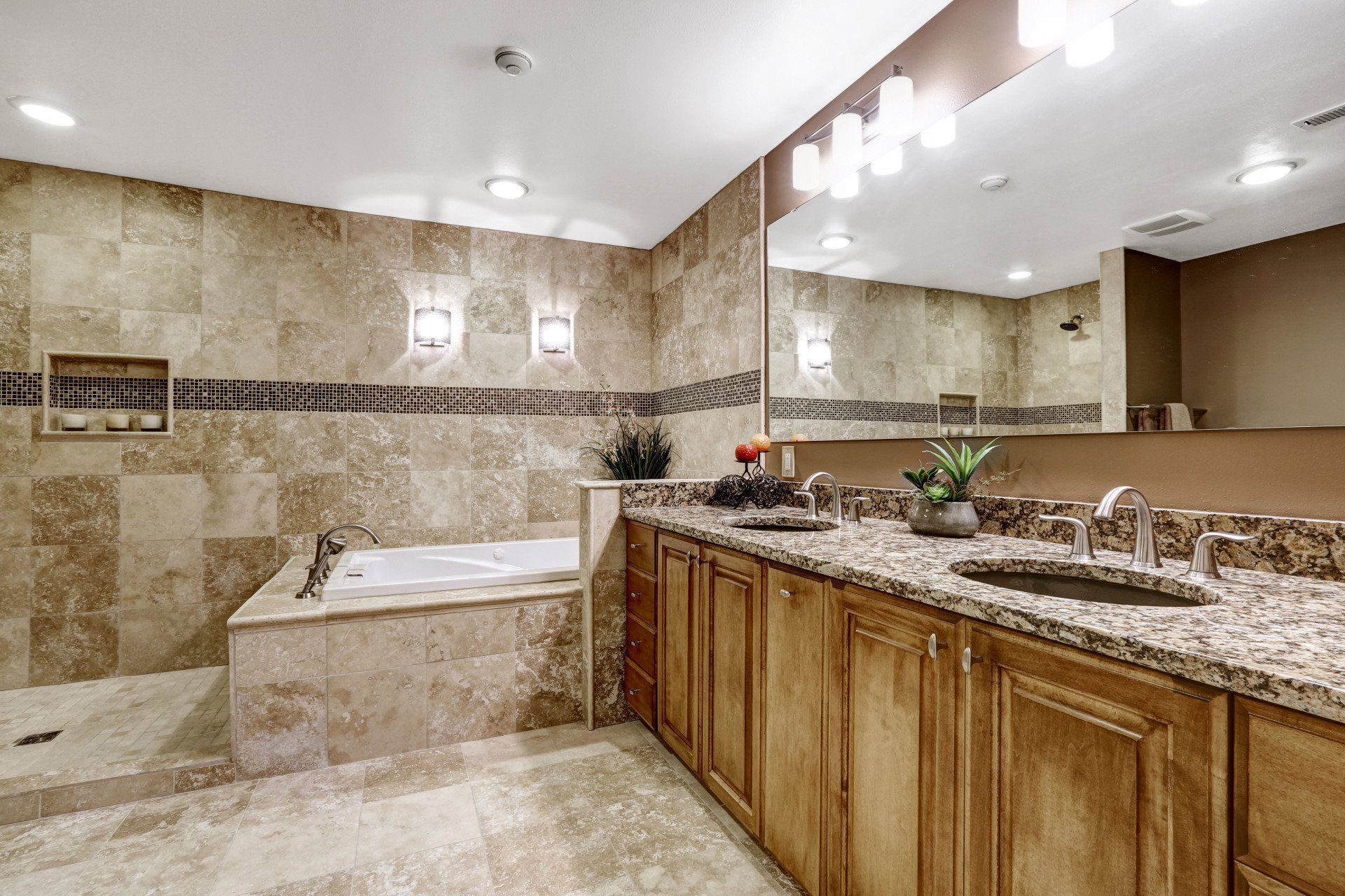 Bathroom with tiled walls, granite countertop, wooden cabinets, tub, shower, and large mirror.