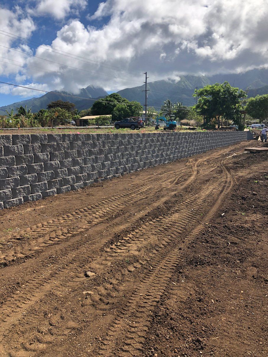 A large stone wall is being built in a dirt field with mountains in the background.