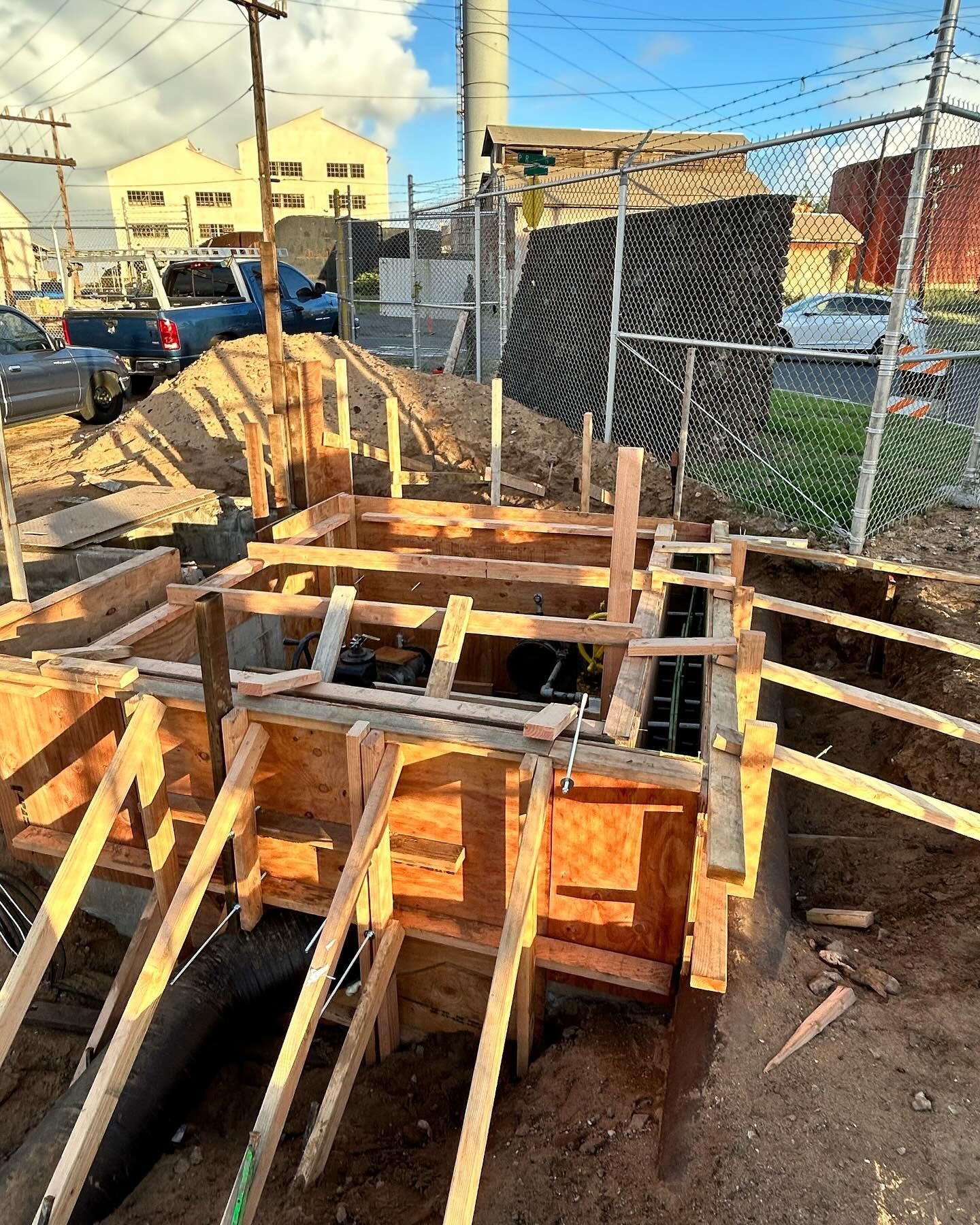 A wooden structure is being built in the dirt next to a chain link fence.