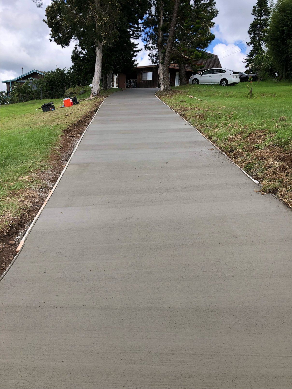 A concrete driveway leading to a house with cars parked on the side of it.