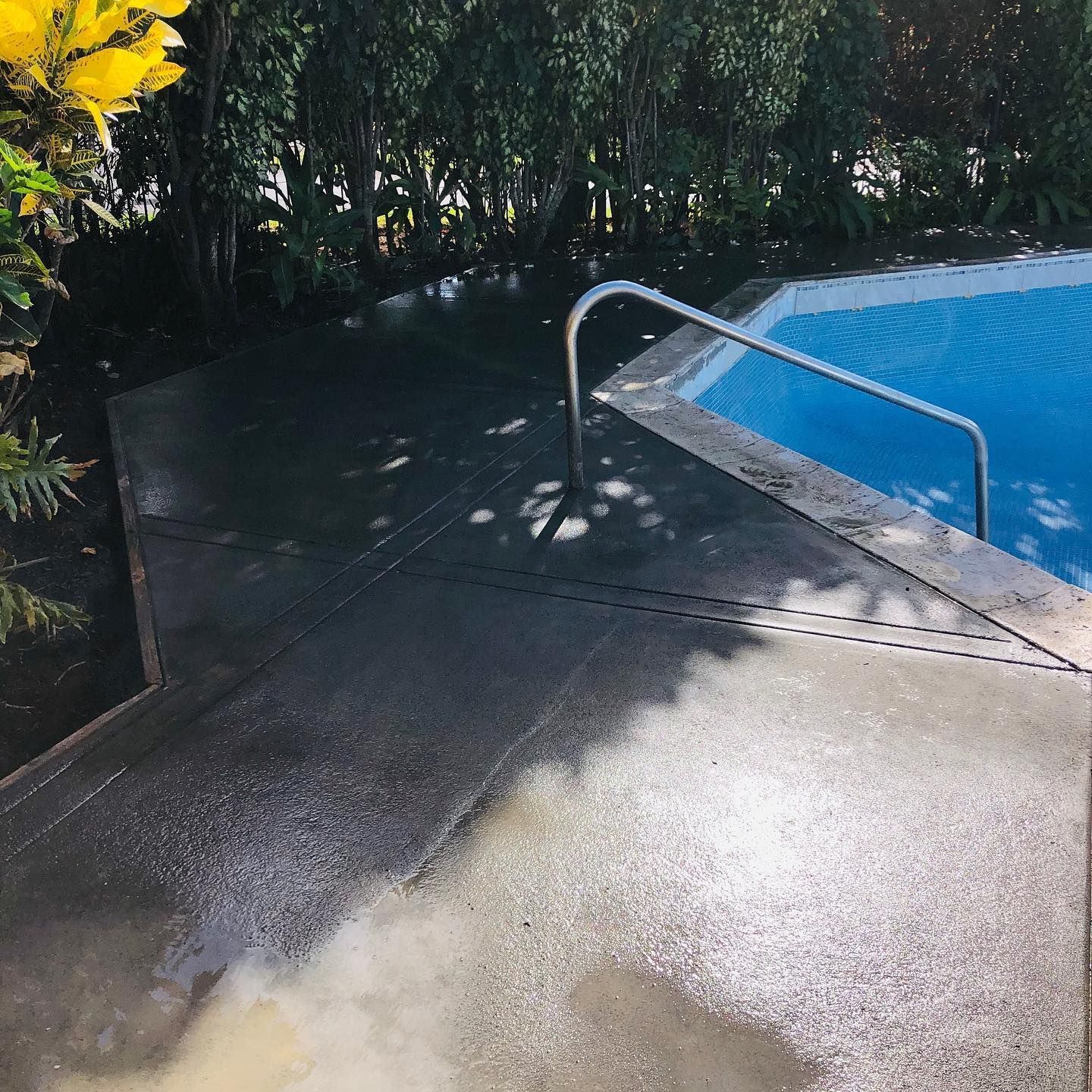 A concrete walkway leading to a swimming pool with a metal railing.