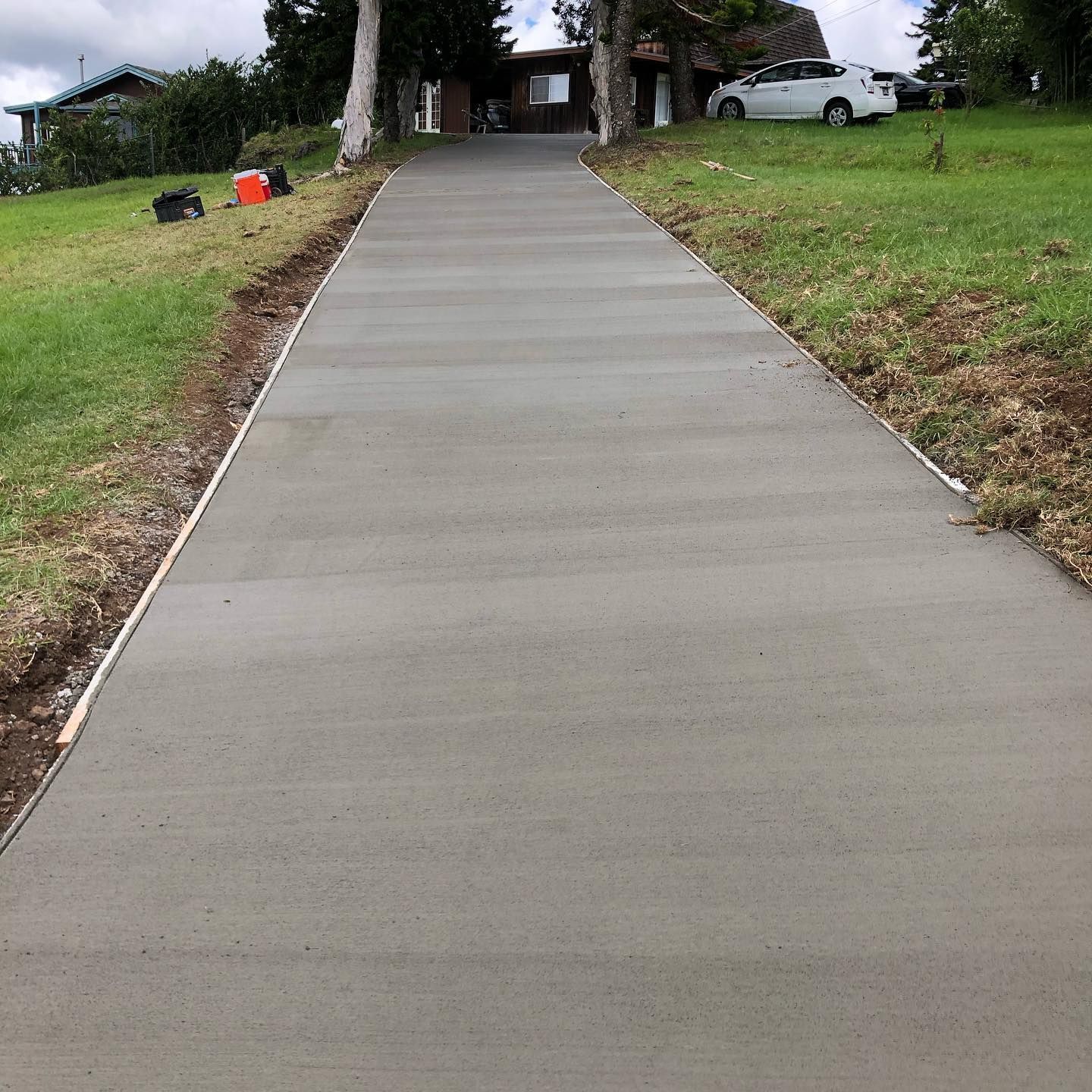 A concrete driveway leading to a house with a white car parked on the side of it.