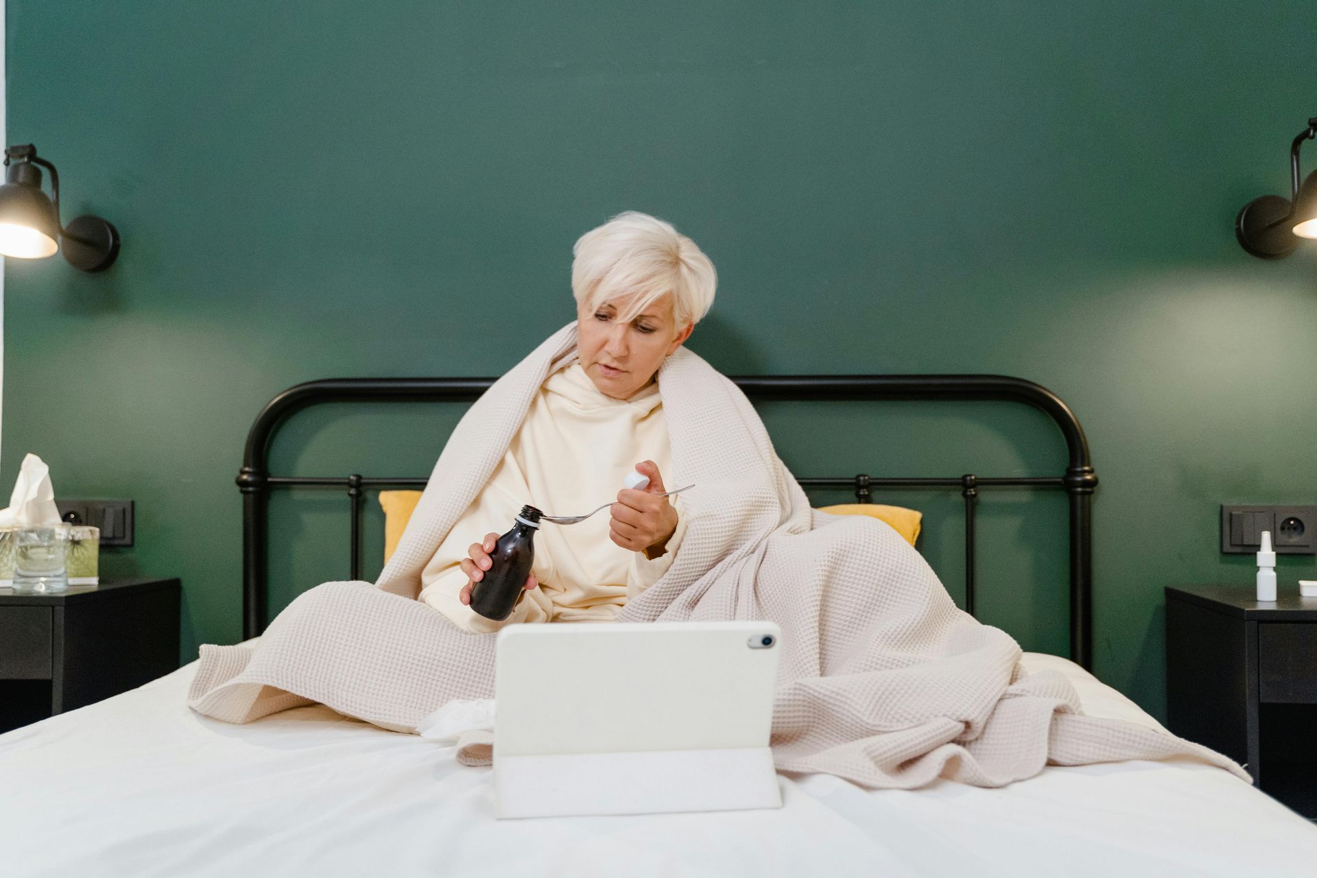 An elderly woman is sitting on a bed using a tablet computer.