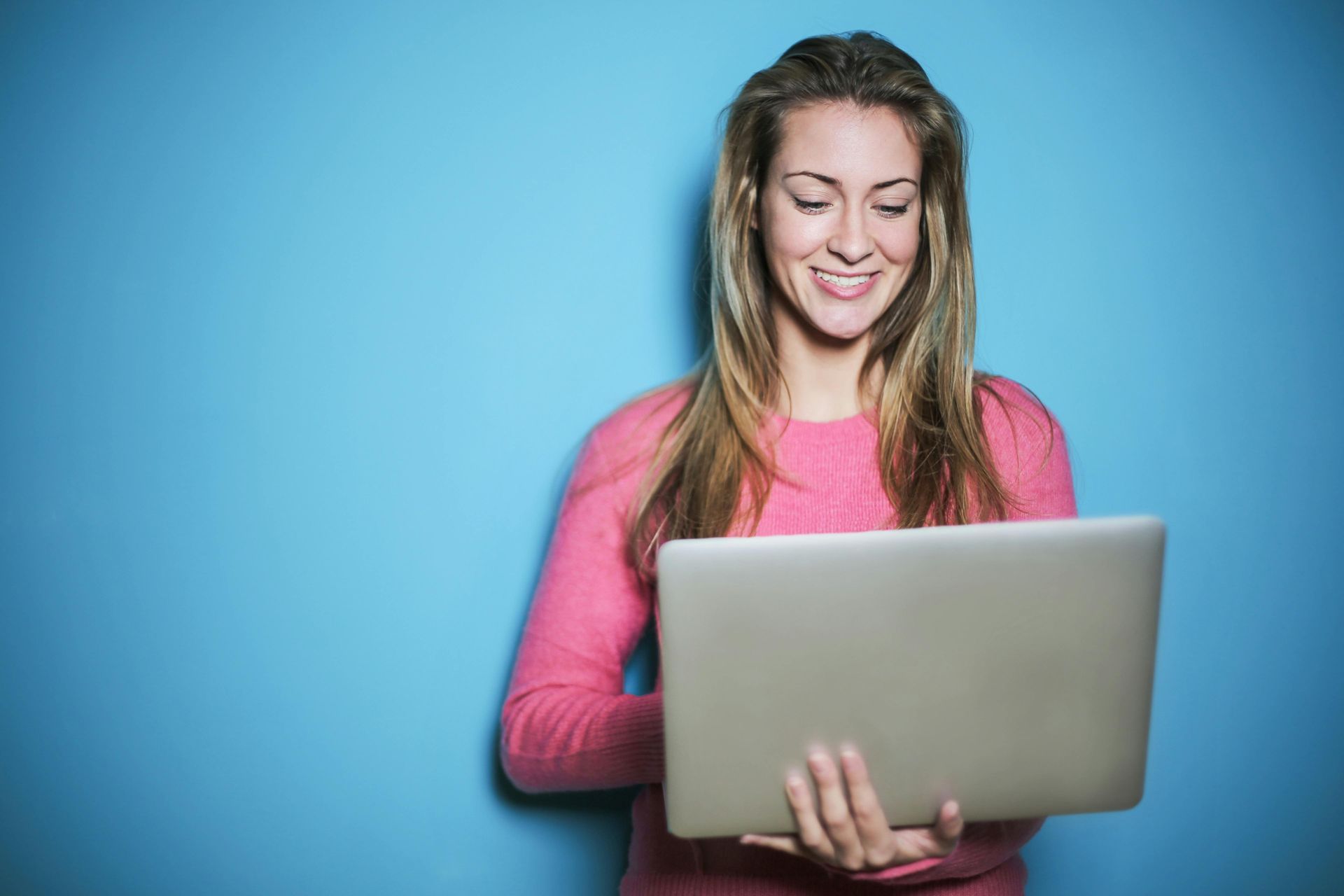 A woman is holding a laptop computer in her hands and smiling.