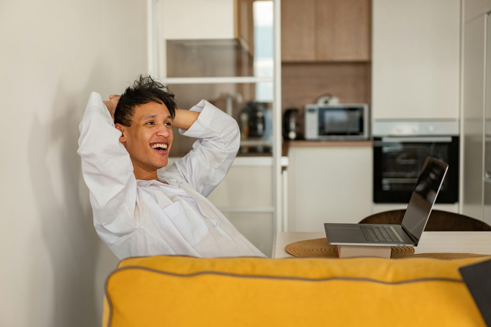 A man is sitting on a yellow couch in front of a laptop computer.