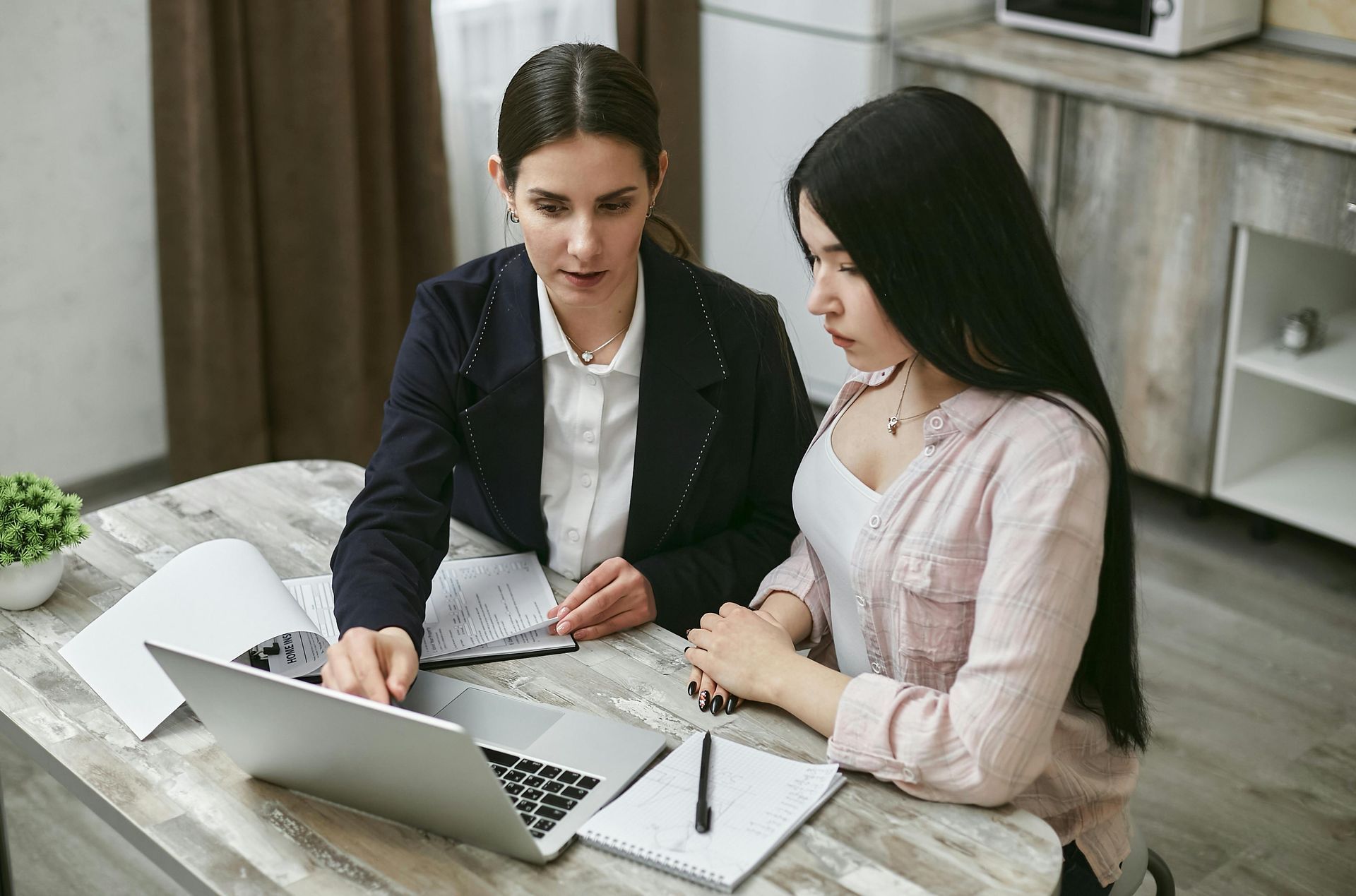 Two women are sitting at a table looking at a laptop computer.