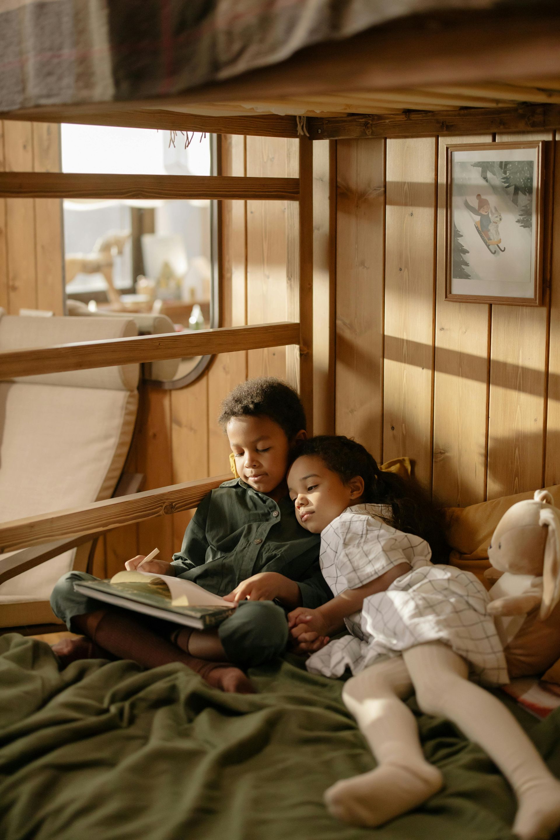 A boy and a girl are sitting on a bunk bed reading a book.