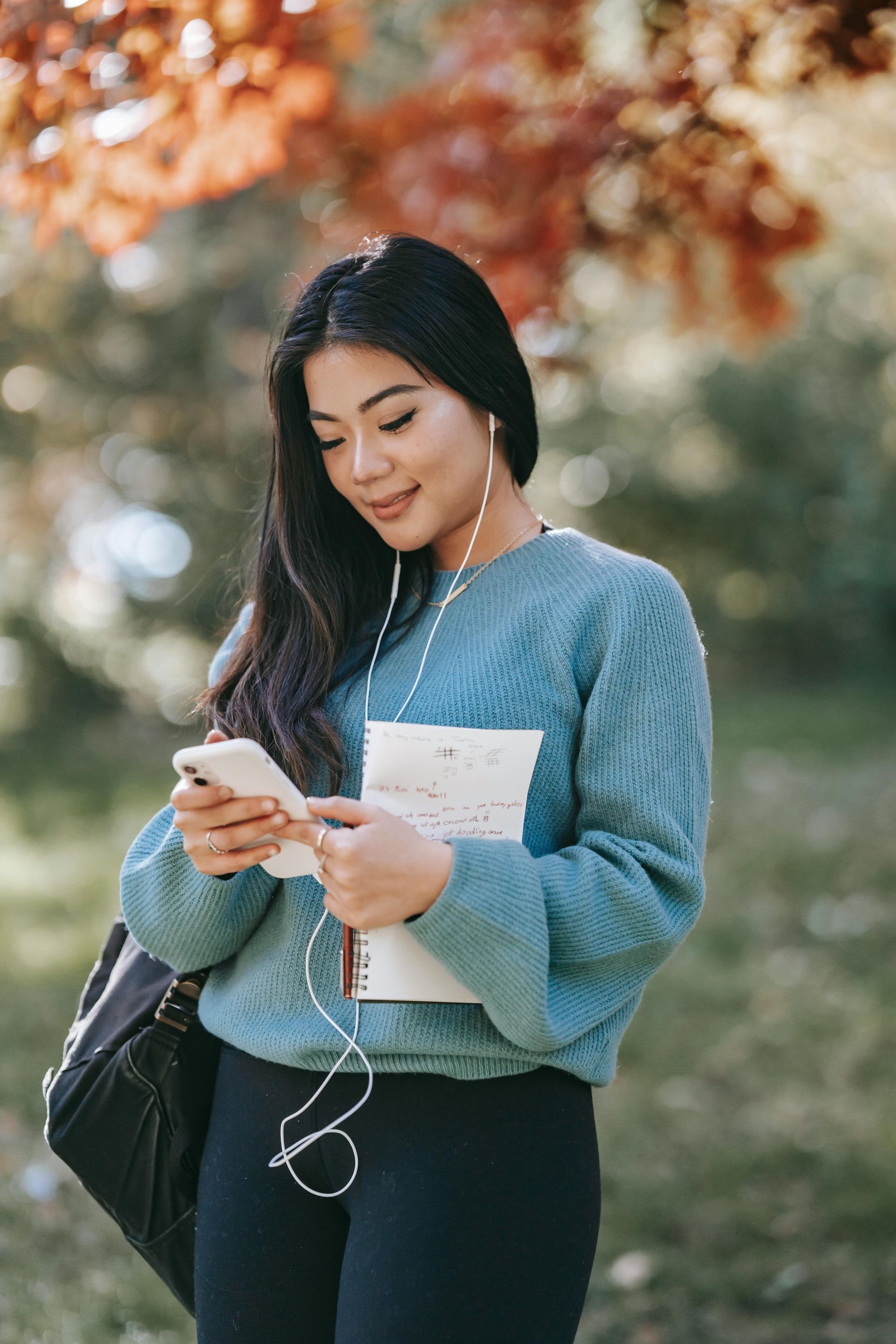 A woman in a blue sweater is listening to music on her phone.