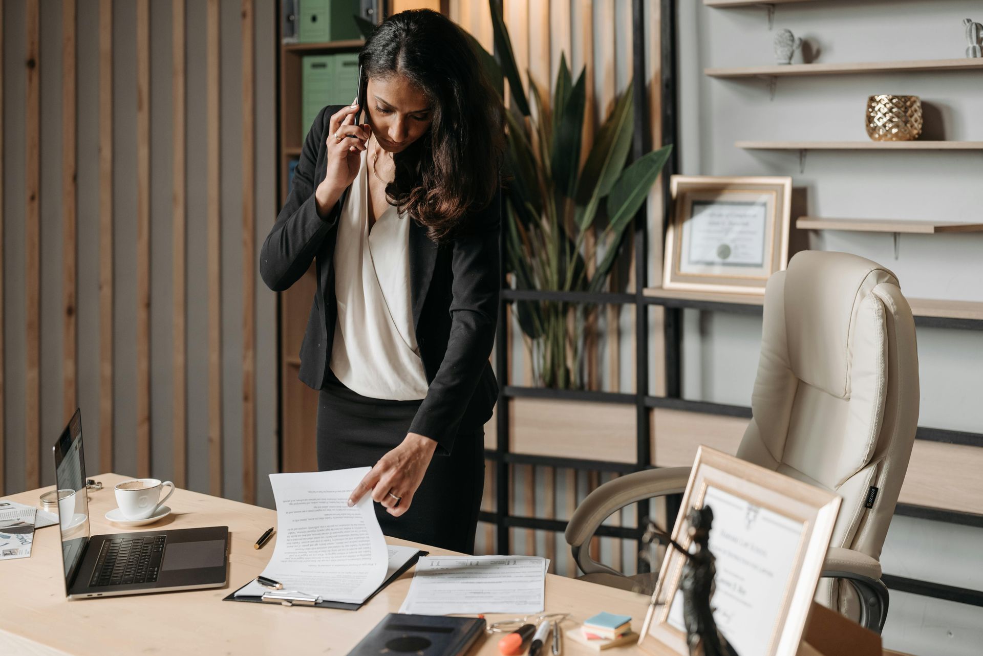 A woman is standing at a desk talking on a cell phone.