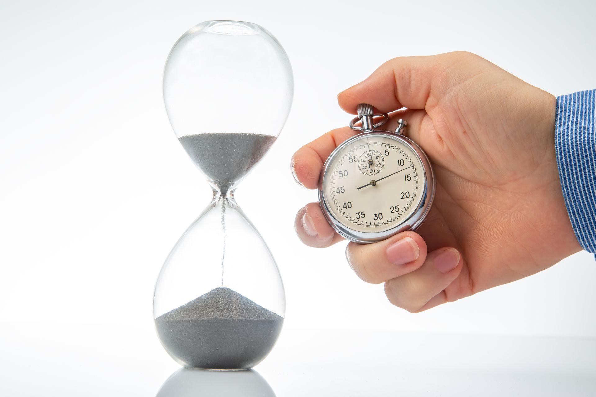 A person is holding a stopwatch in front of an hourglass.