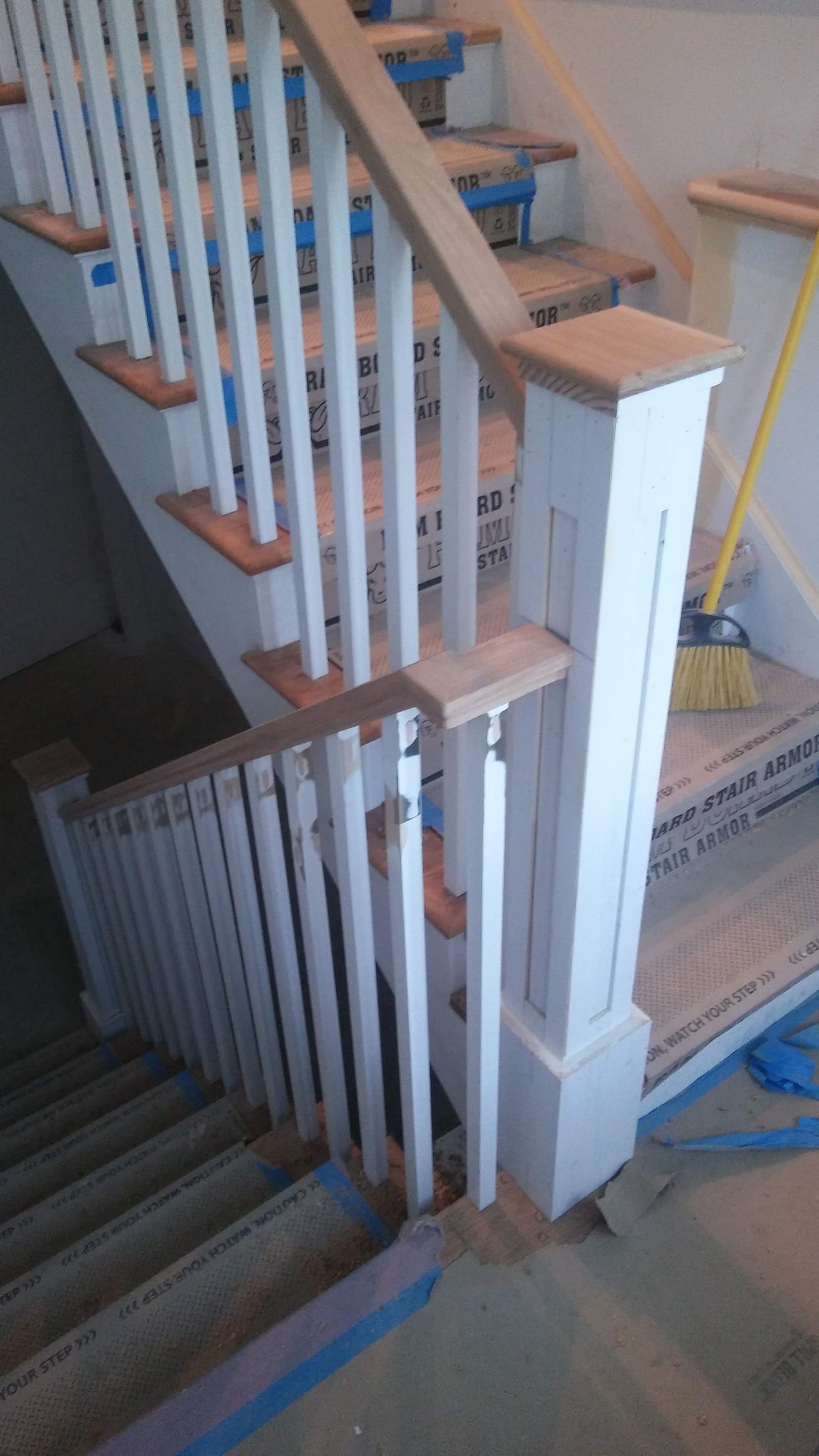 A staircase with a white railing and wooden steps is being painted.