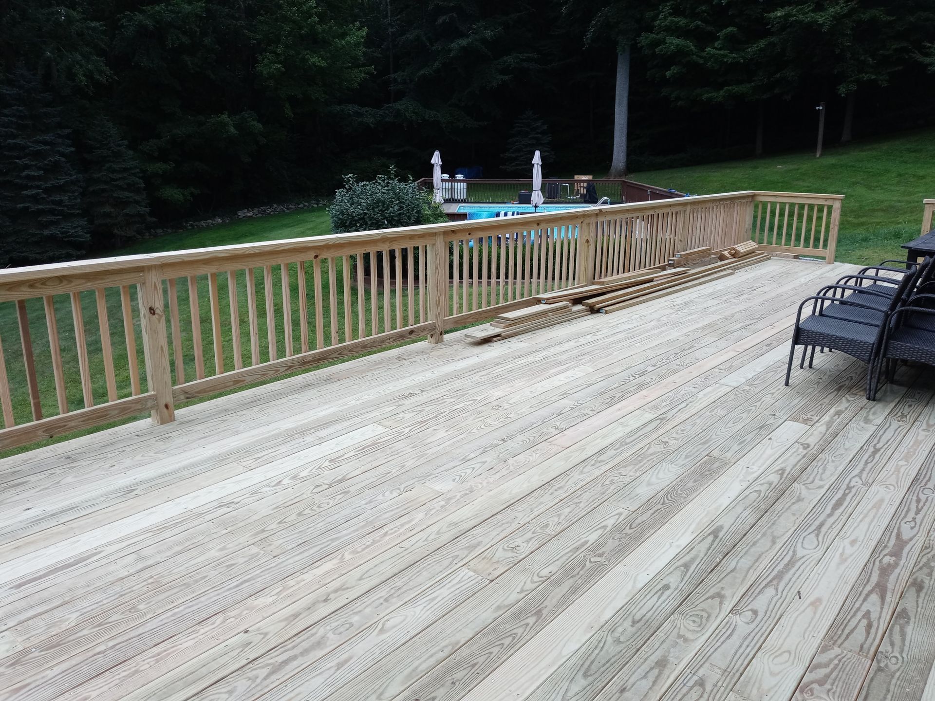 A large wooden deck with a fence and a pool in the background.