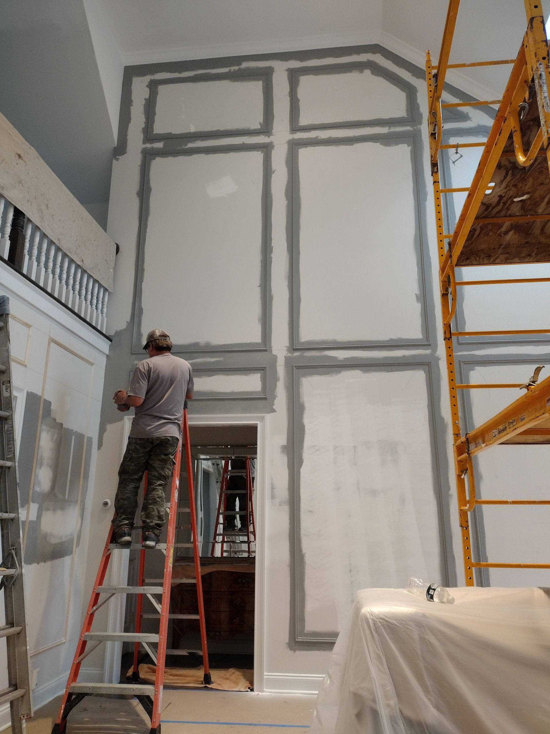 A man is standing on a ladder painting a wall.