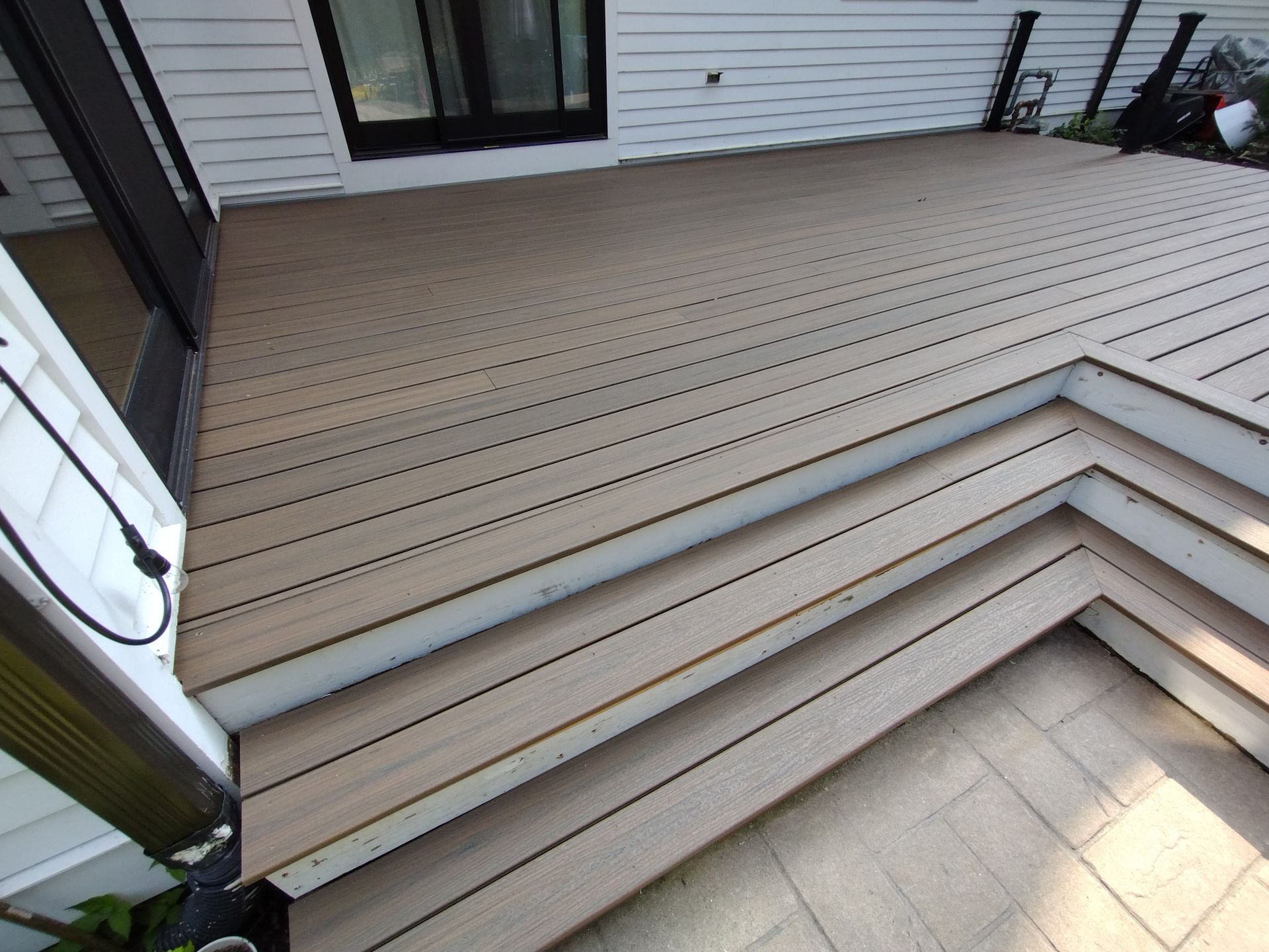 A wooden deck with stairs leading up to it and a white house in the background.