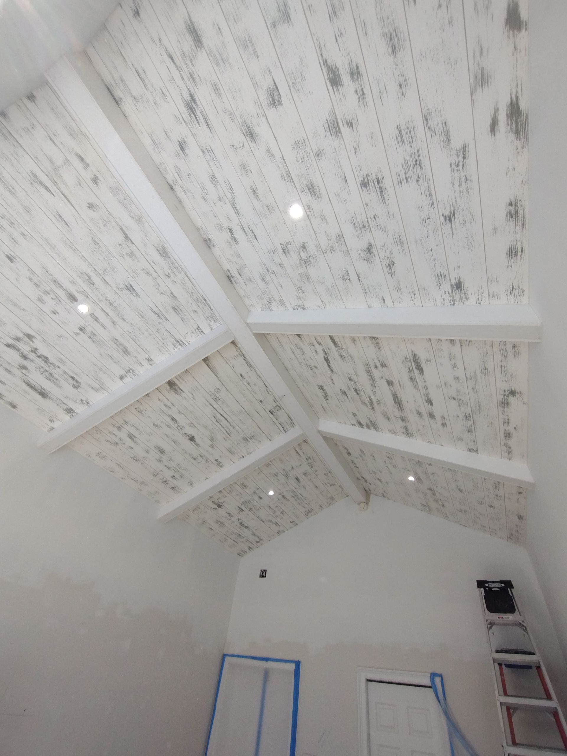 A white ceiling with a vaulted ceiling in a room with a ladder.