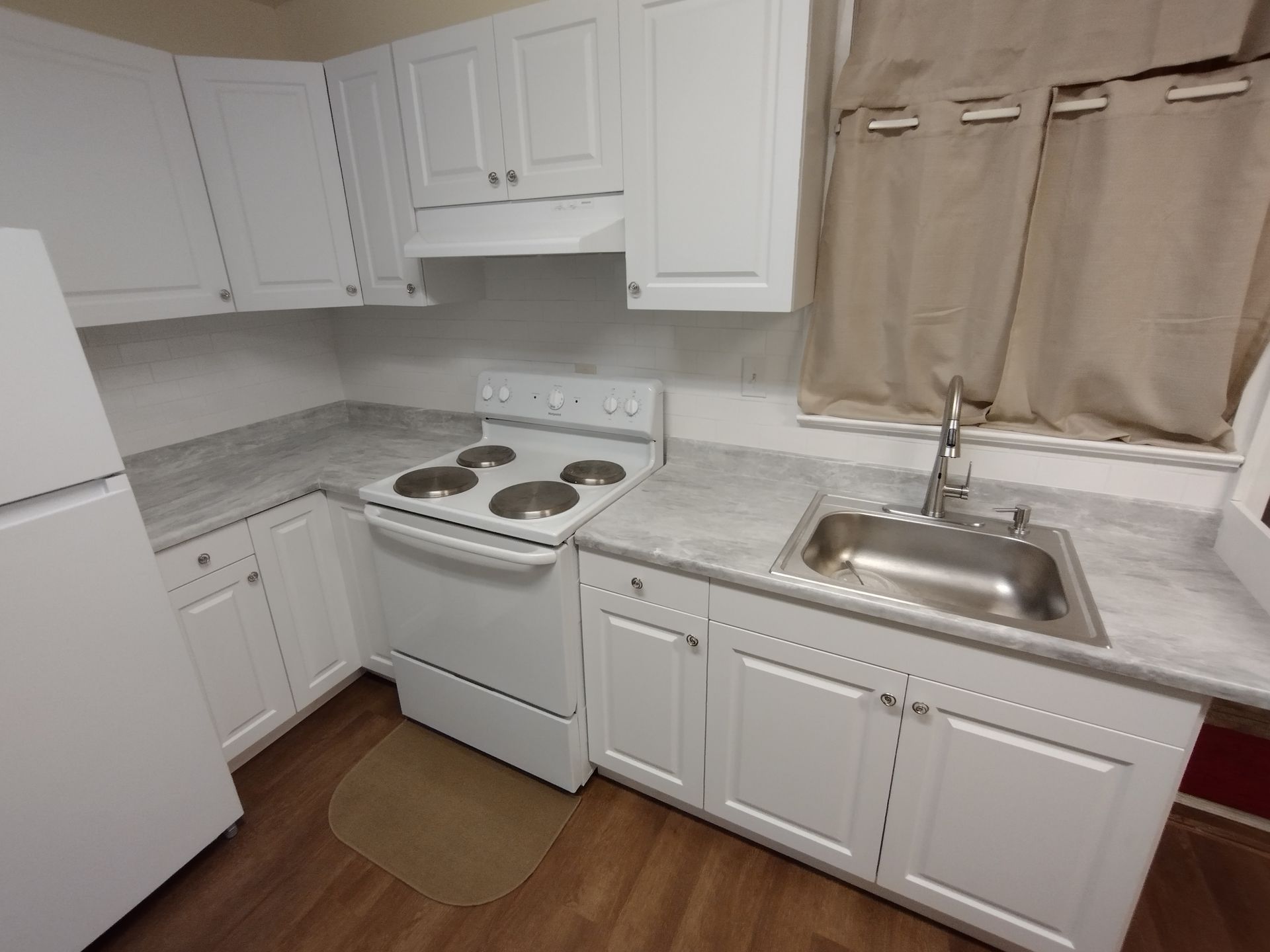 A kitchen with white cabinets , a stove , a sink and a refrigerator.