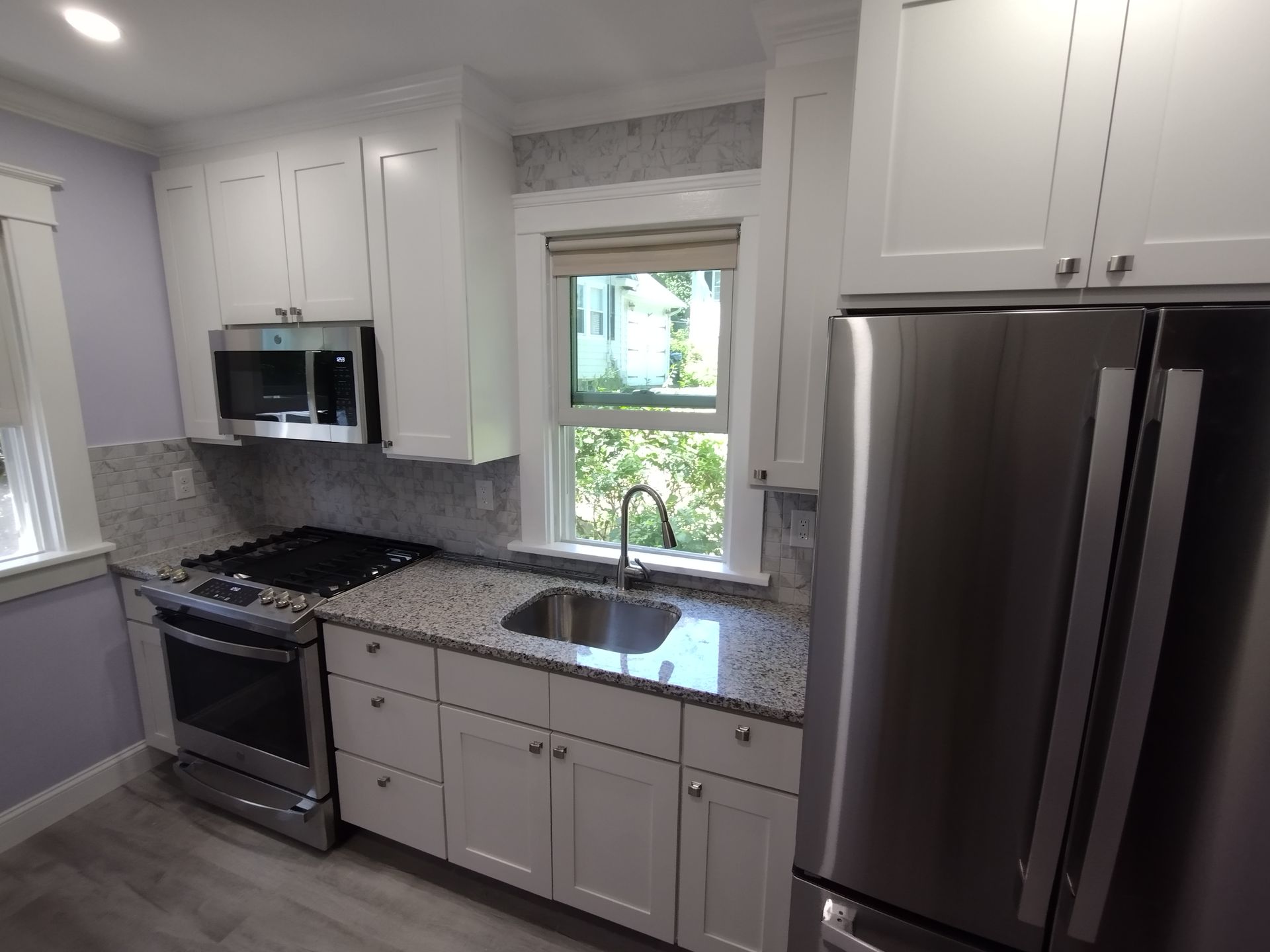 A kitchen with white cabinets , stainless steel appliances , a sink , stove and refrigerator.
