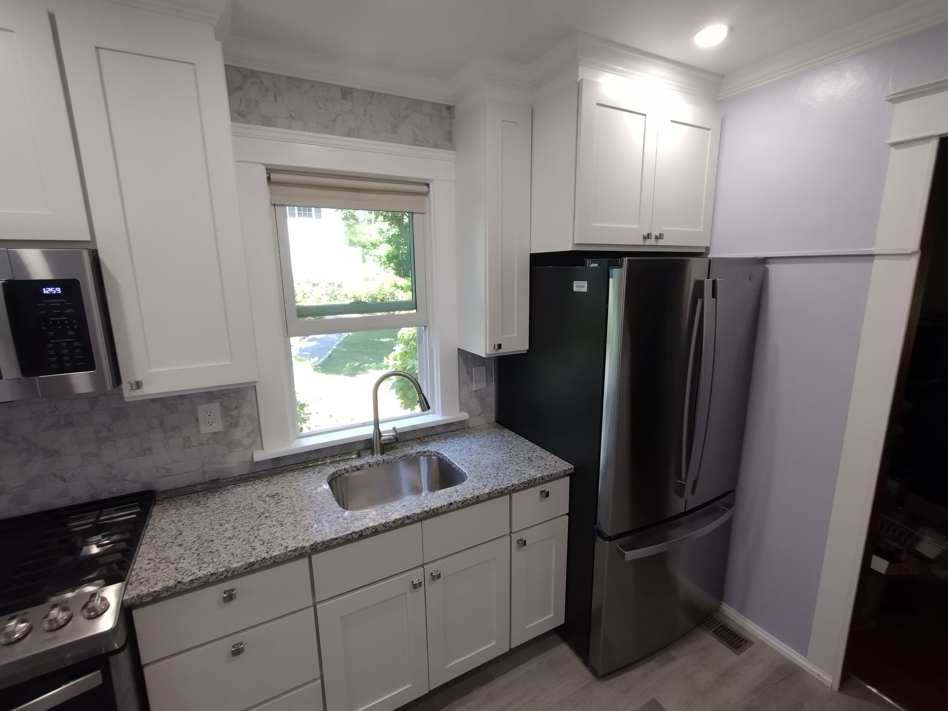 A kitchen with white cabinets , granite counter tops , stainless steel appliances and a stainless steel refrigerator.