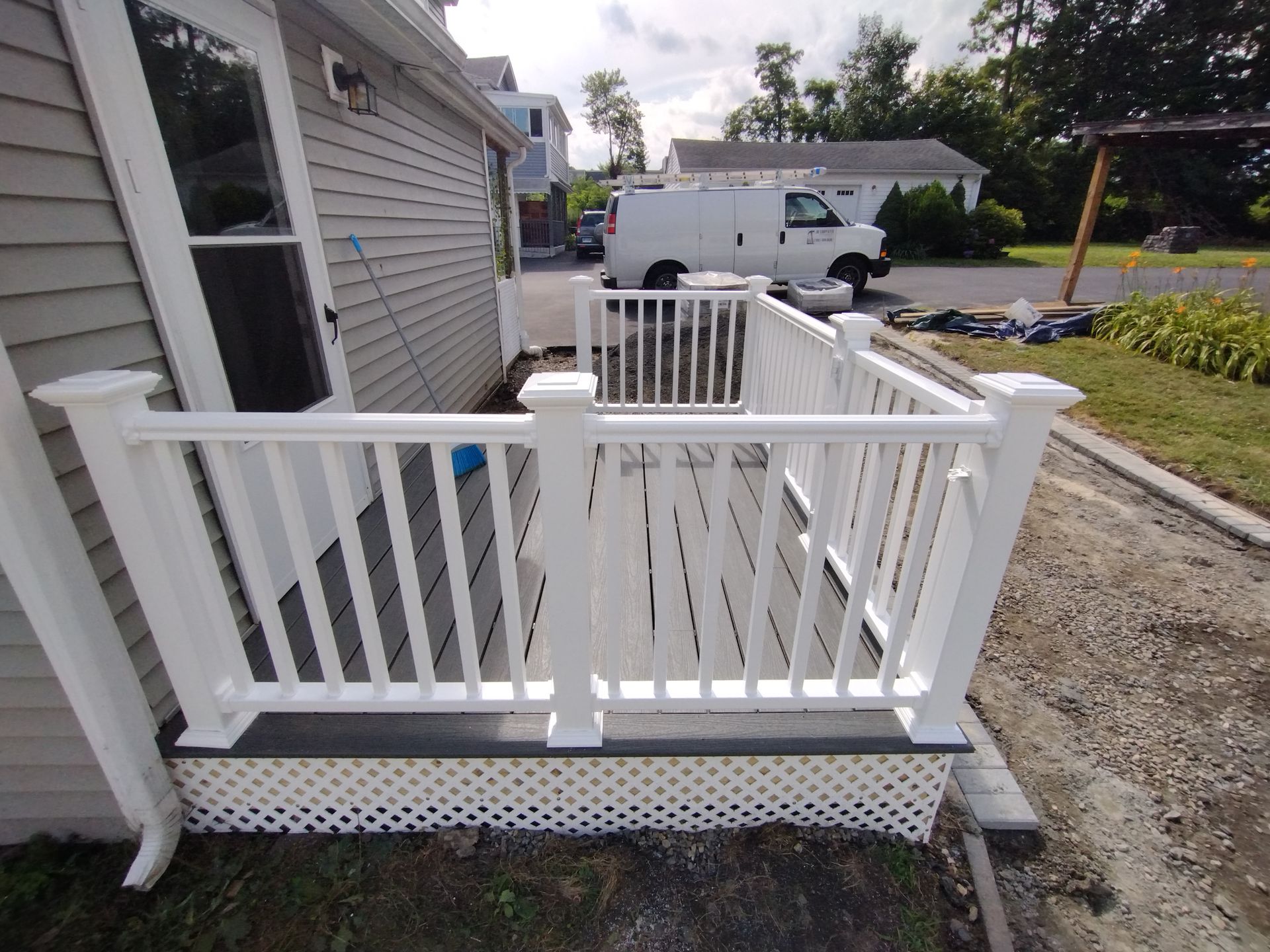 A white van is parked in front of a house with a white railing.