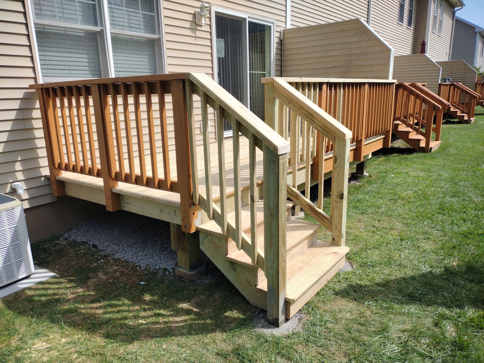 A wooden deck with stairs leading up to it is in front of a house.