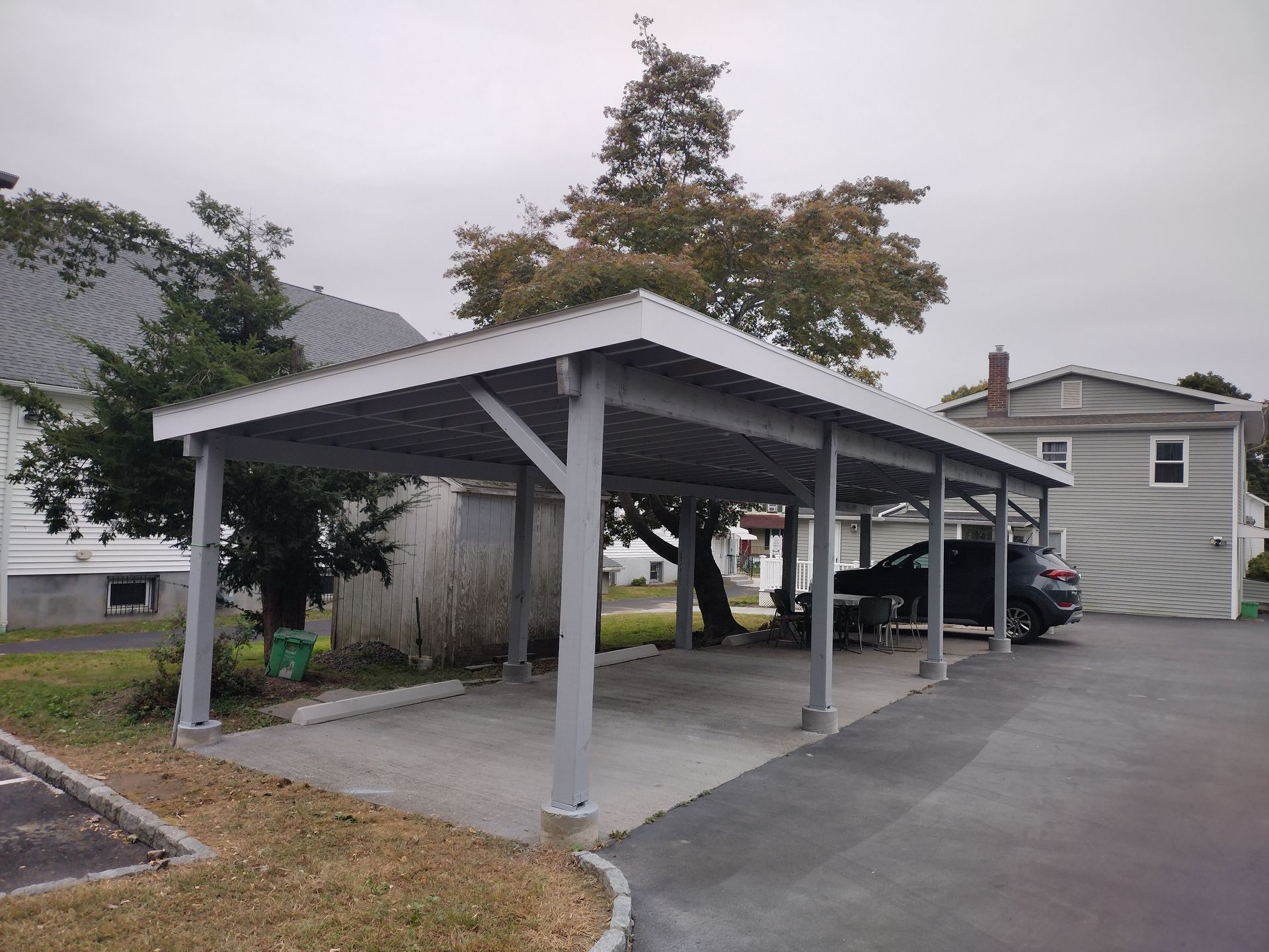 A carport with a car parked underneath it in front of a house.