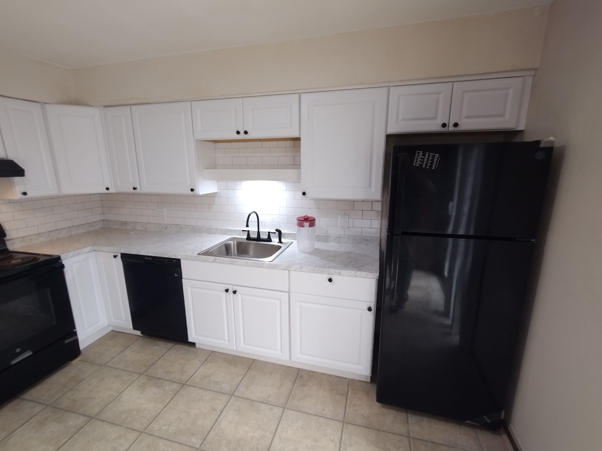 A kitchen with white cabinets and a black refrigerator