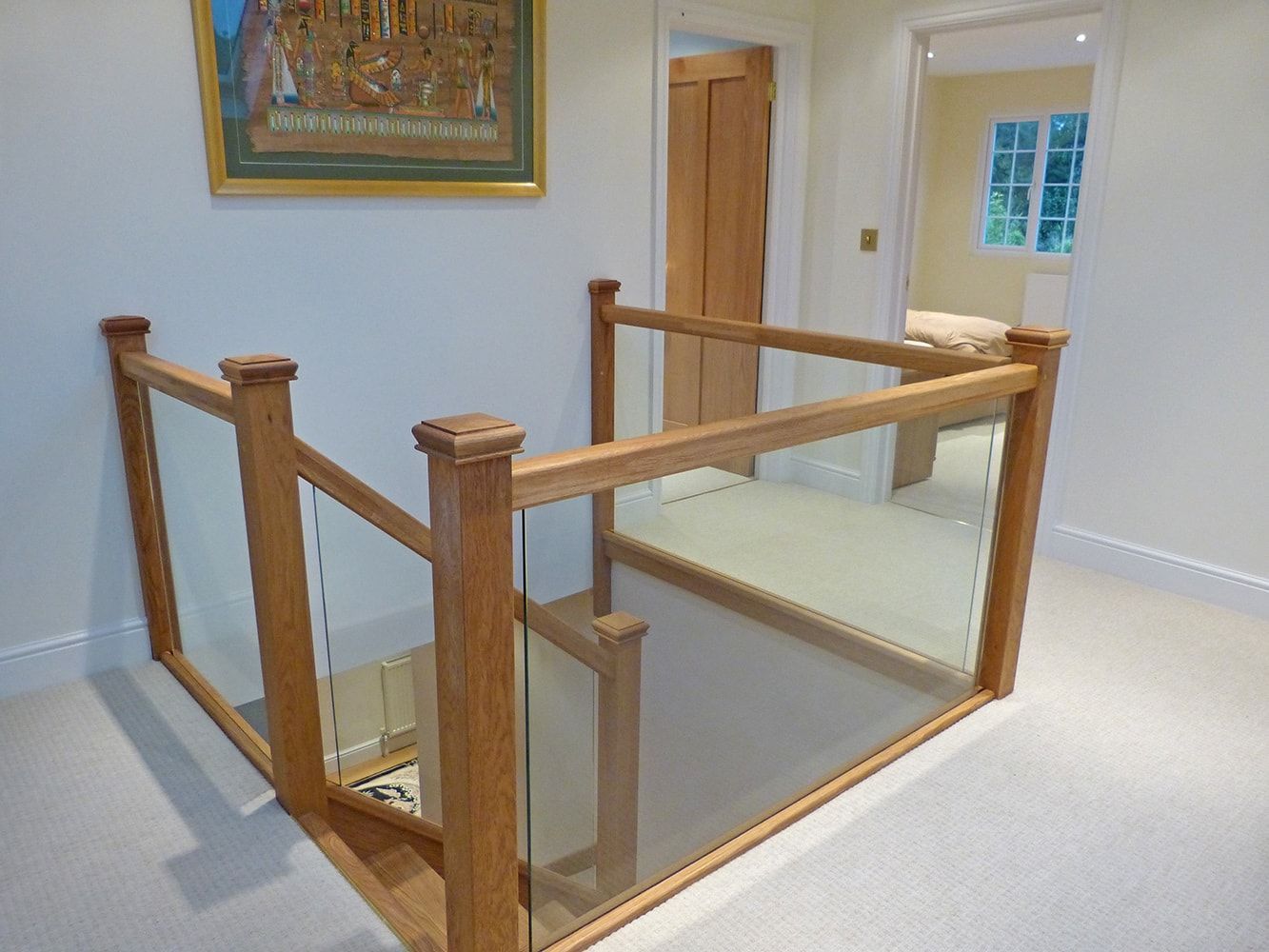 A wooden staircase with a glass railing and a picture on the wall.