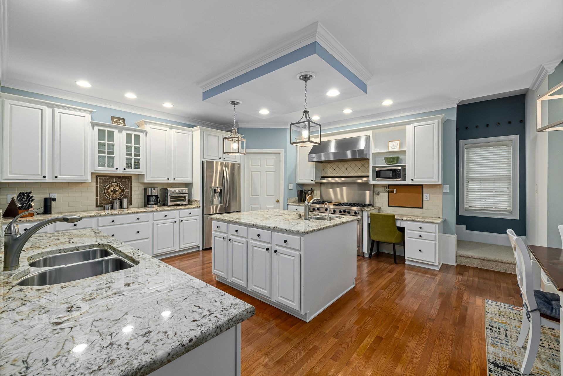 A kitchen with white cabinets , granite counter tops , stainless steel appliances and a large island.