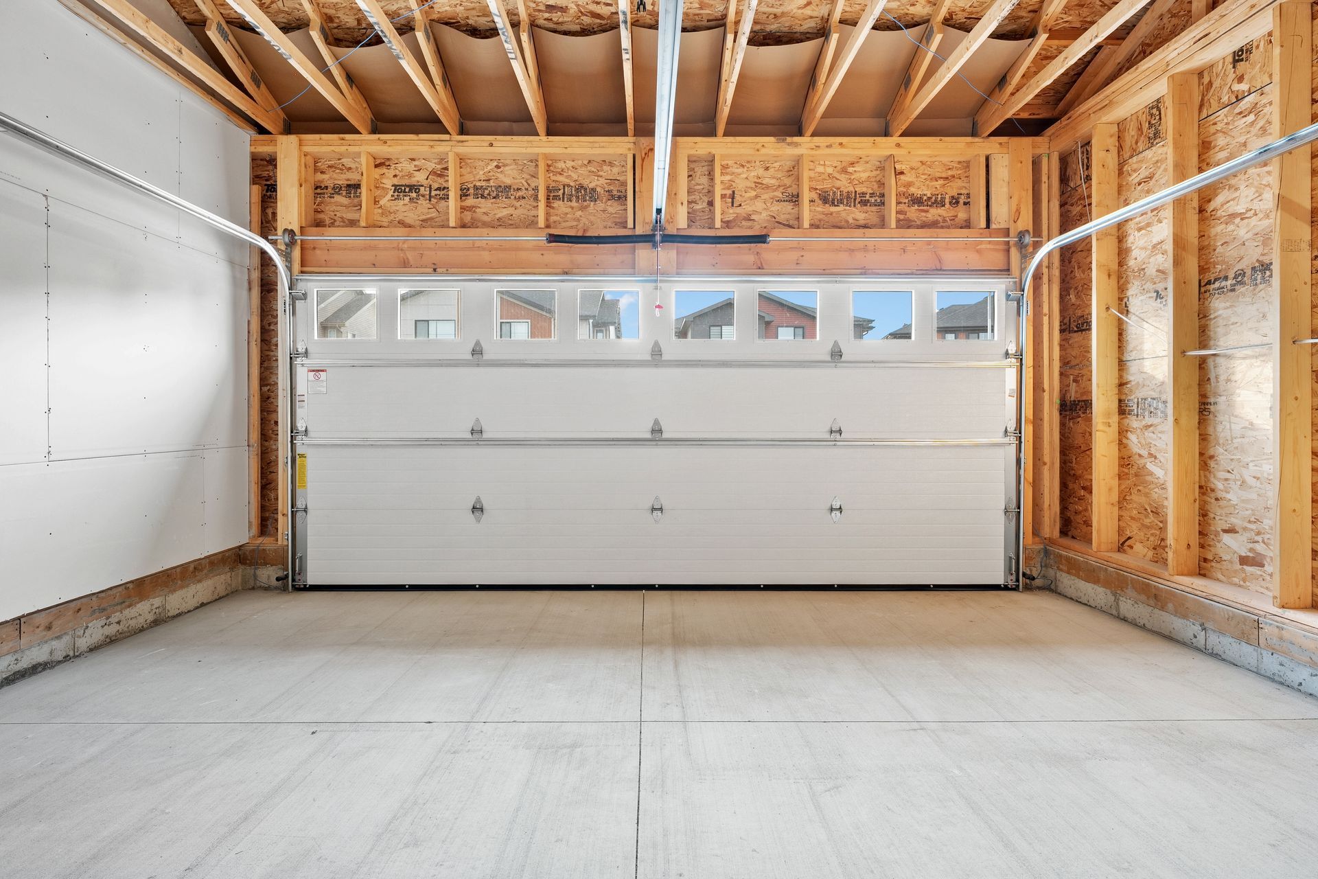An empty garage with a white garage door and wooden walls.