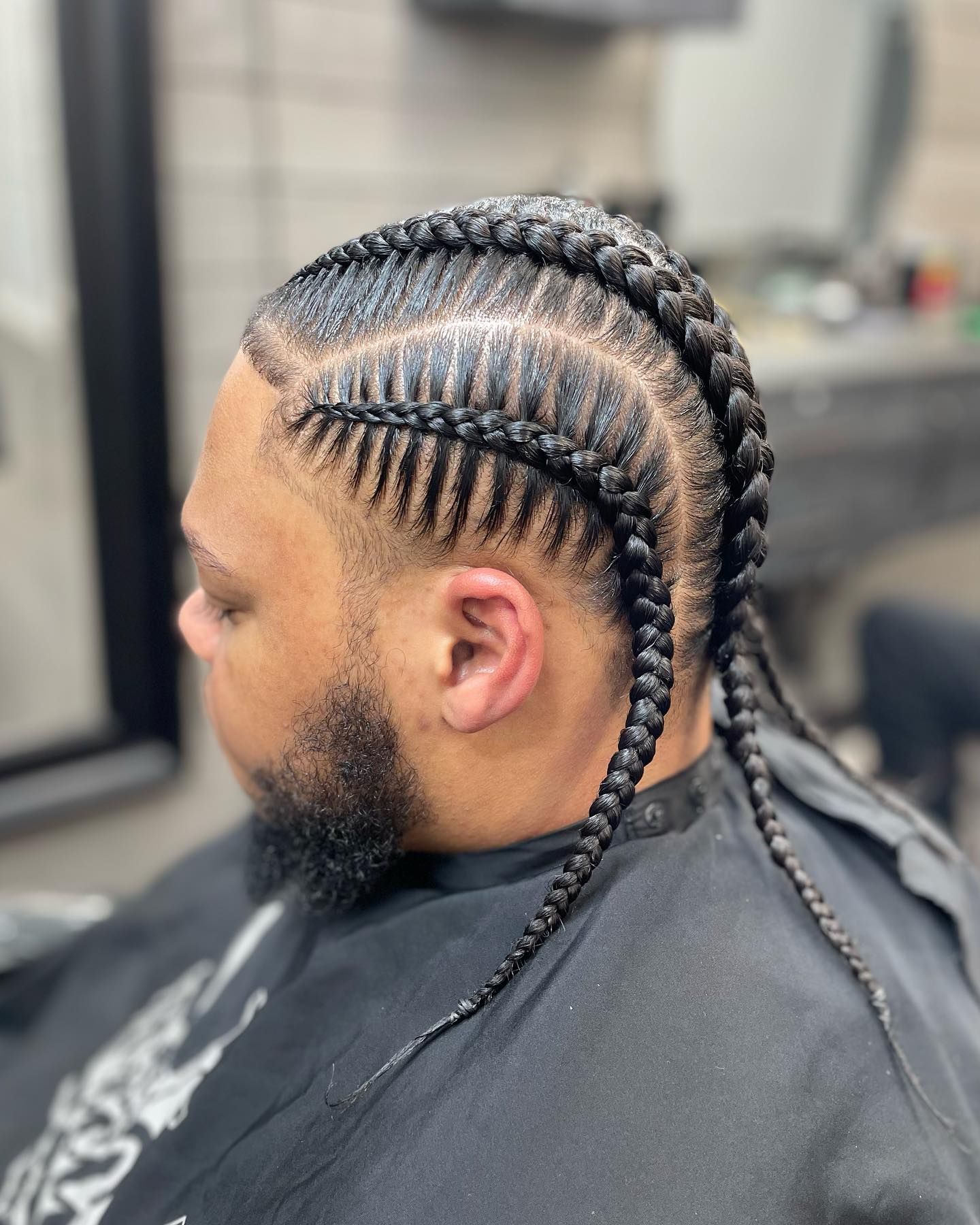 A man with a beard is getting his hair braided in a barber shop.