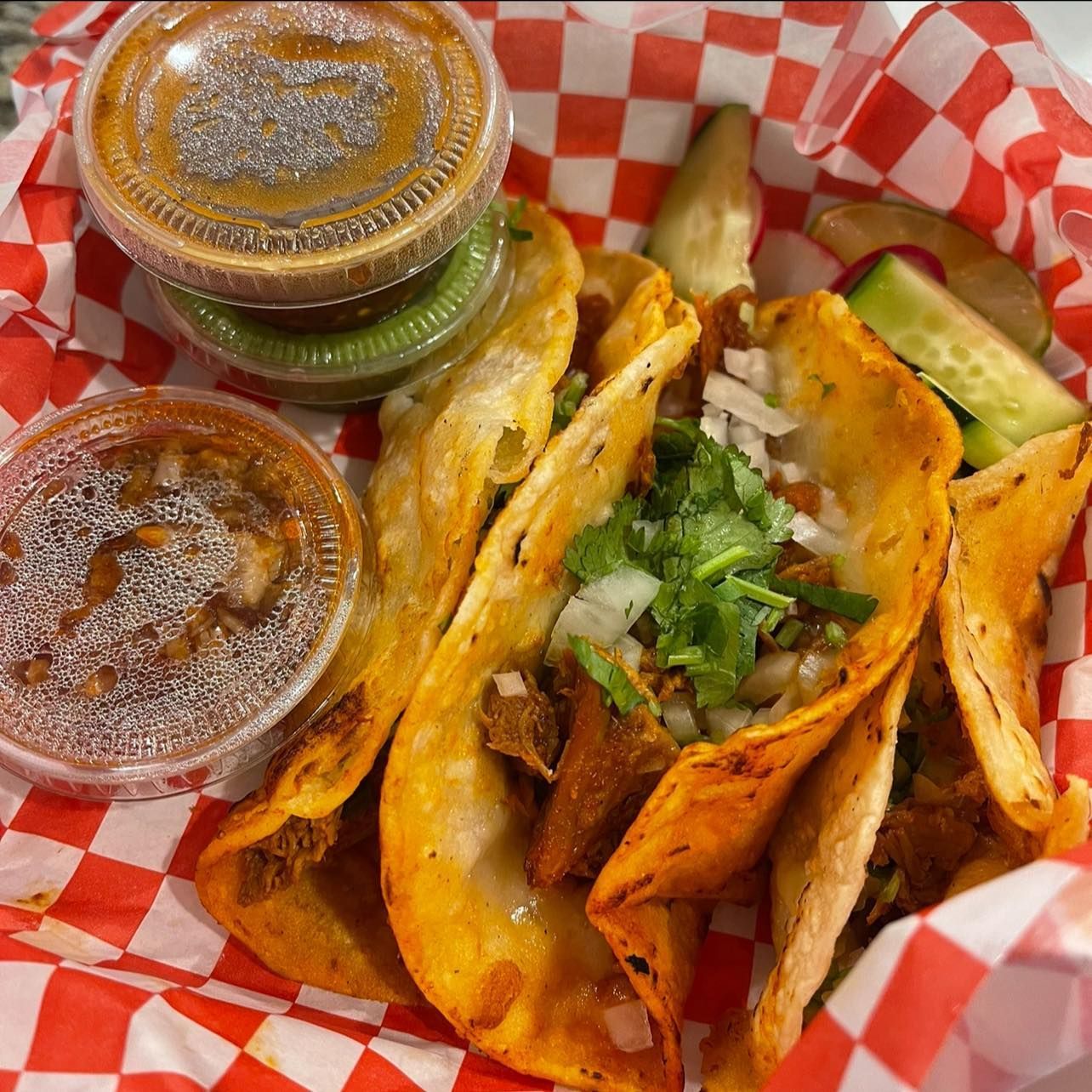 A basket of tacos with sauces and vegetables on a checkered paper.