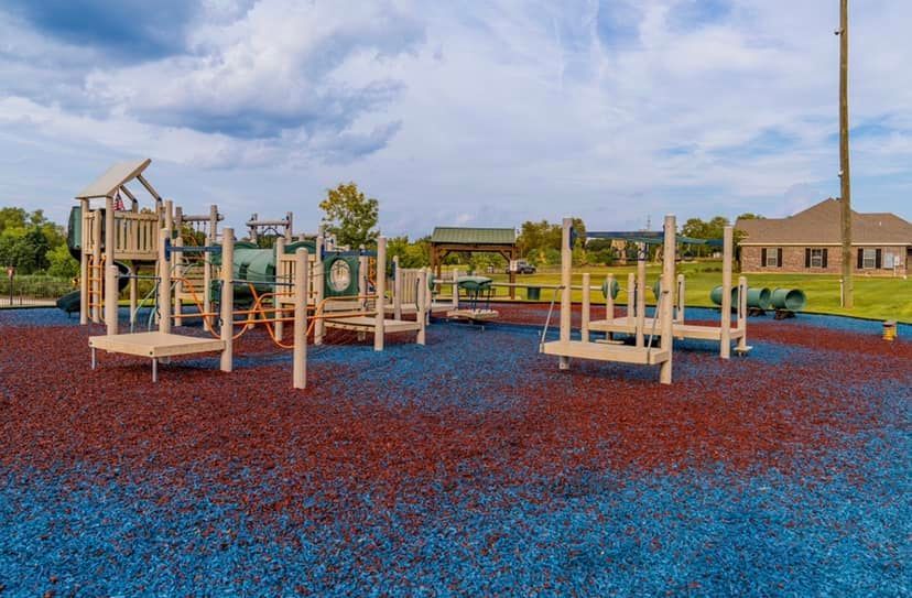 A playground with blue and red mulch and a house in the background.