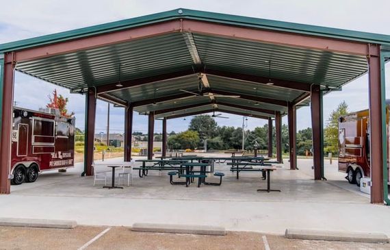 Two food trucks are parked under a covered area with picnic tables.