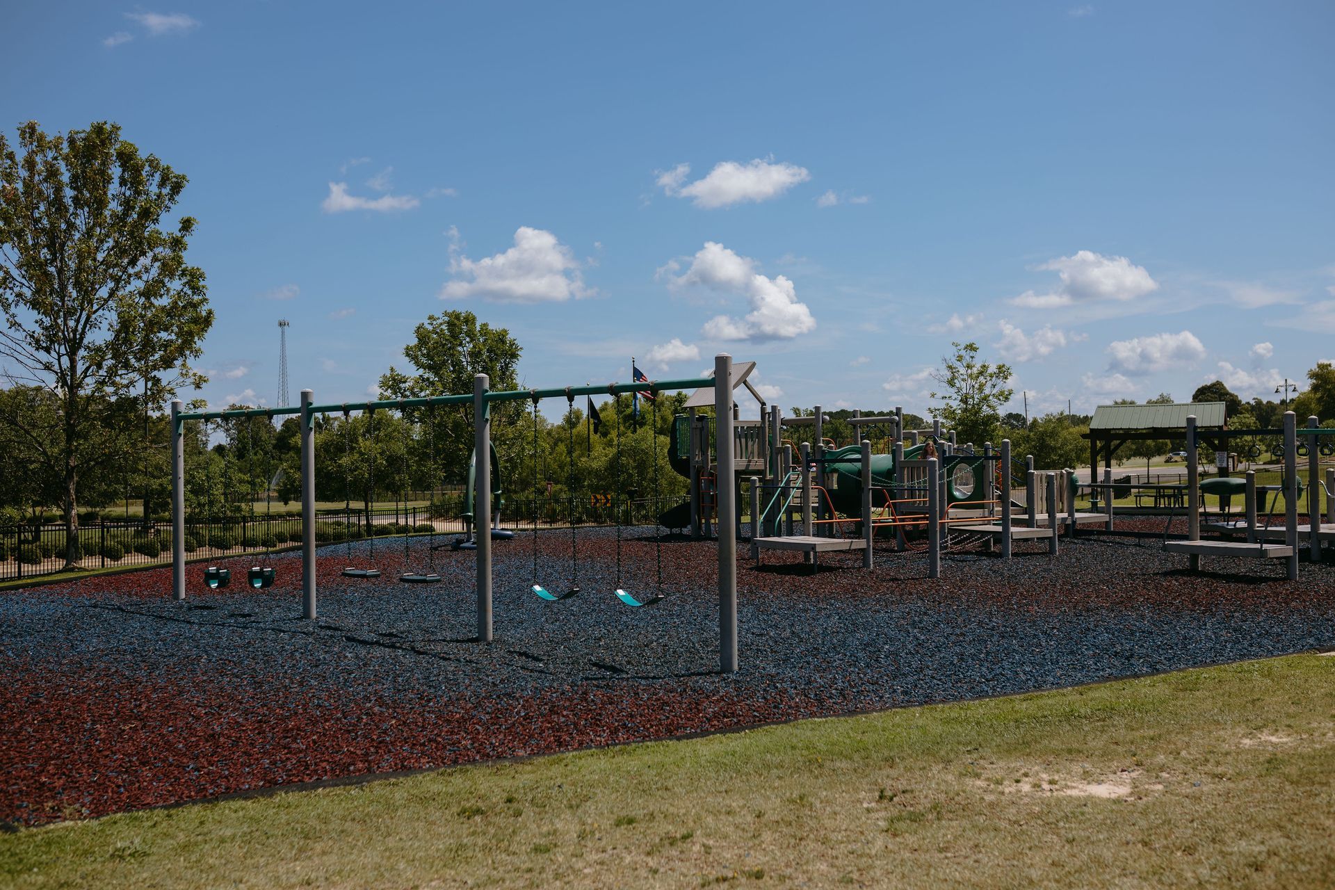 A playground with blue and red mulch and a house in the background.