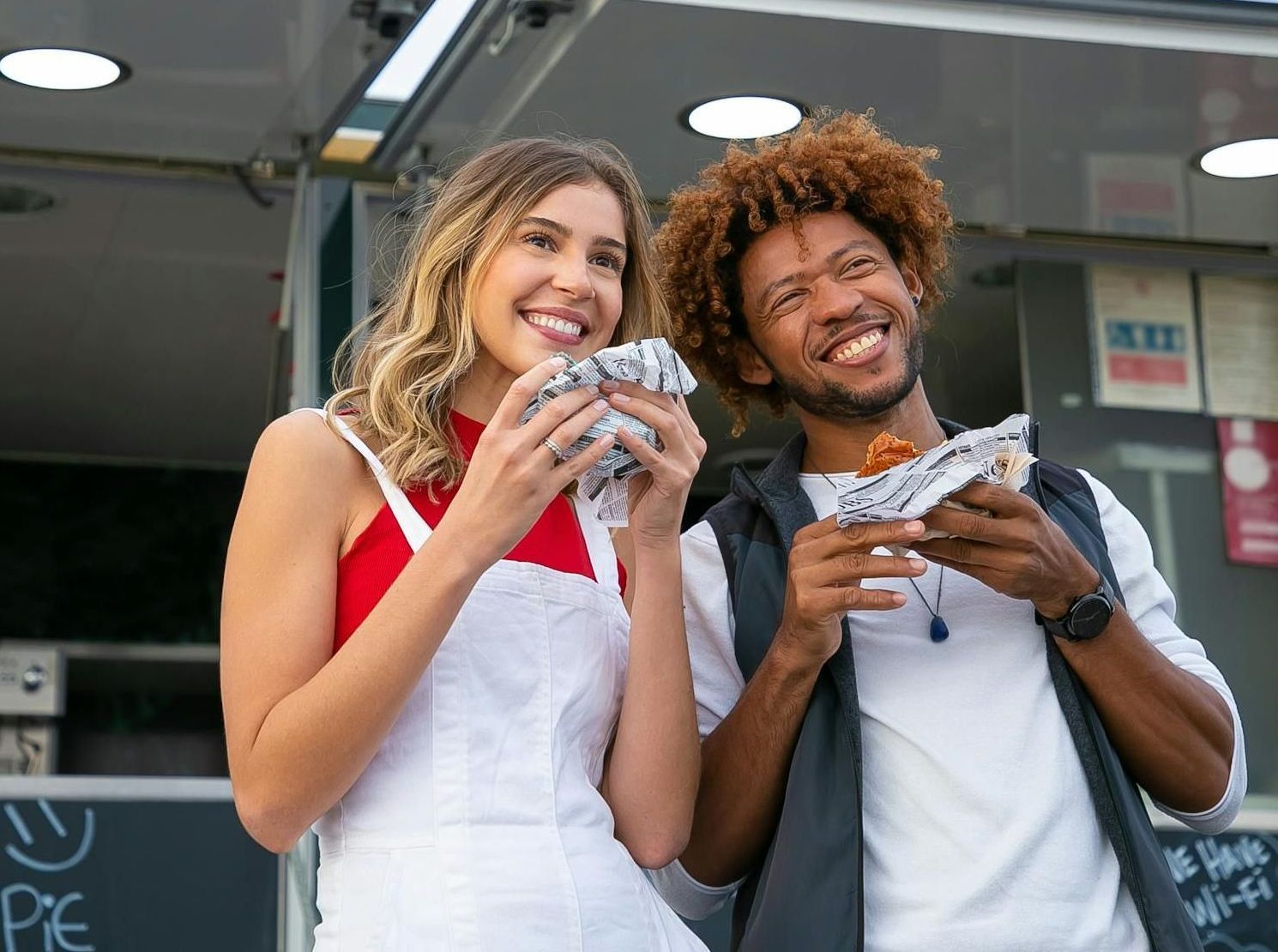 A man and a woman are eating food from a food truck.