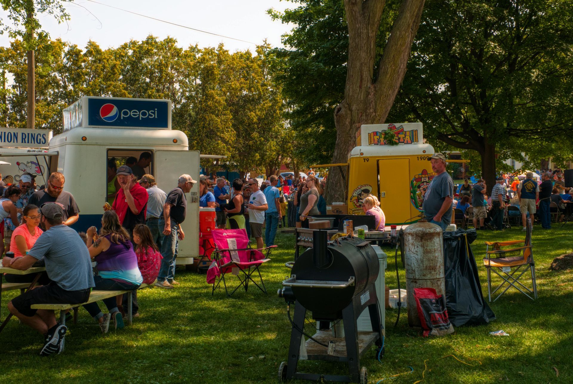 A group of people are gathered in a park with a pepsi truck in the background