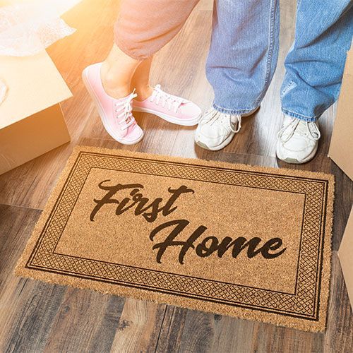 A couple is standing next to a first home doormat.