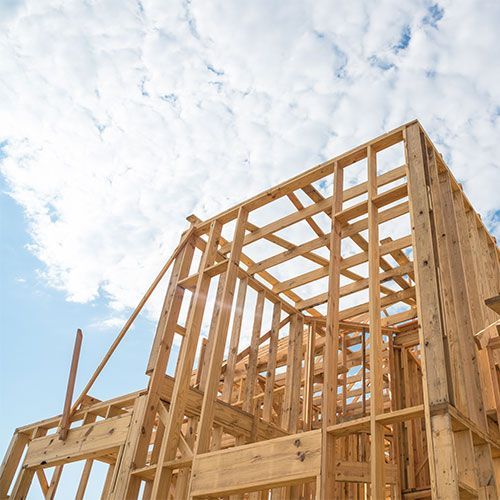 A wooden house is being built with a blue sky in the background.