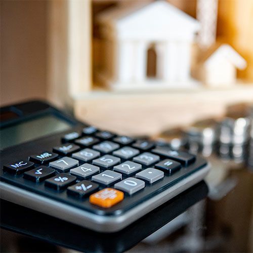 A calculator is sitting on a table in front of a model house and several piles of coins.