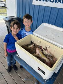 Two boys smile next to an open cooler filled with fish on a dock.