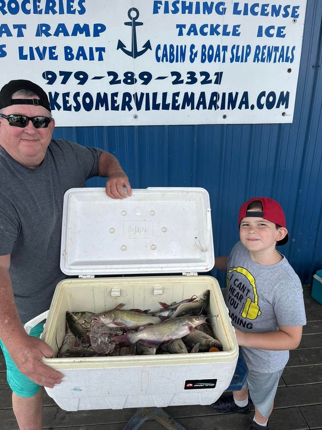 Man and boy holding a cooler filled with fish at a marina.