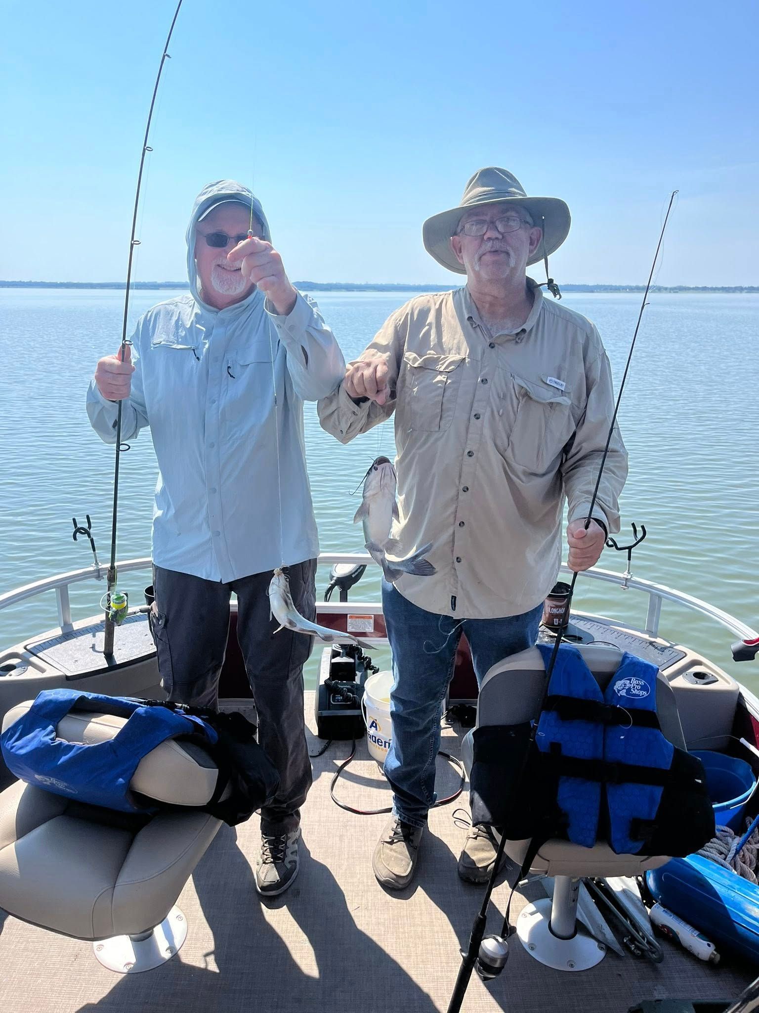 Two men on a boat, holding up fish they caught, blue sky and water.